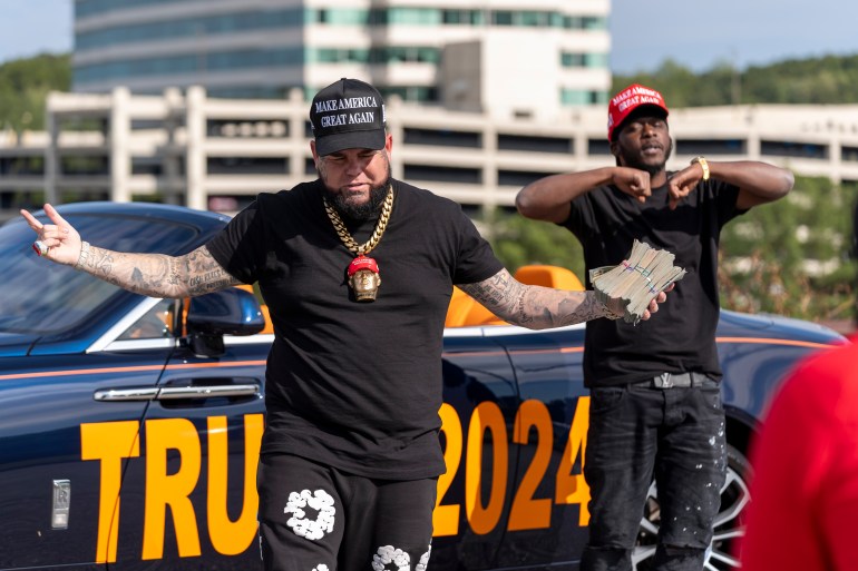 Forgiato Blow, left, and Therealblackdonaldtrump film a music video in the parking lot before Republican presidential nominee former President Donald Trump speaks at a campaign event at the Cobb Energy Performing Arts Centre, Tuesday, Oct. 15, 2024, in Atlanta. (AP Photo/Alex Brandon)