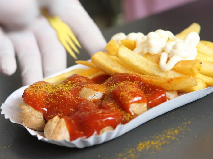 BERLIN, GERMANY - JULY 14: An employee puts a small plastic fork into a plate of currywurst with french fries at Konnopke's currywurst stand on July 14, 2012 in Berlin, Germany. Currywurst, originally founded in post-war Berlin by Herta Heuwa, is Berlin's answer to fast food and is sold at specialized stands across the city and the rest of Germany. Currywurst is pork sausage, with or without casing, fried or deep-fried, that is typically smothered in curry powder and a ketchup-like sauce called curry sauce and served with french fries.