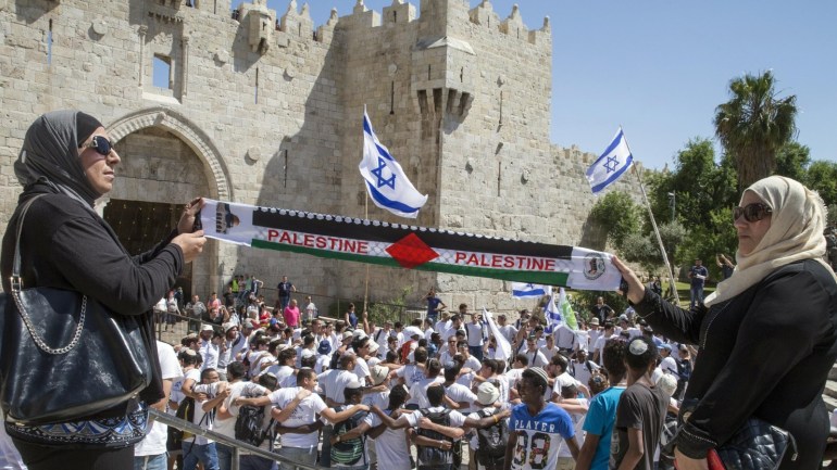 Palestinian women hold a scarf bearing the Palestine name as Israeli youths hold their national flag as they take part in the 'flag march' through Damascus Gate in Jerusalem's old city during celebrations for Jerusalem Day on May 17, 2015 which marks the anniversary of the 'reunification' of the holy city after Israel captured the Arab eastern sector from Jordan during the 1967 Six-Day War. AFP PHOTO / JACK GUEZ